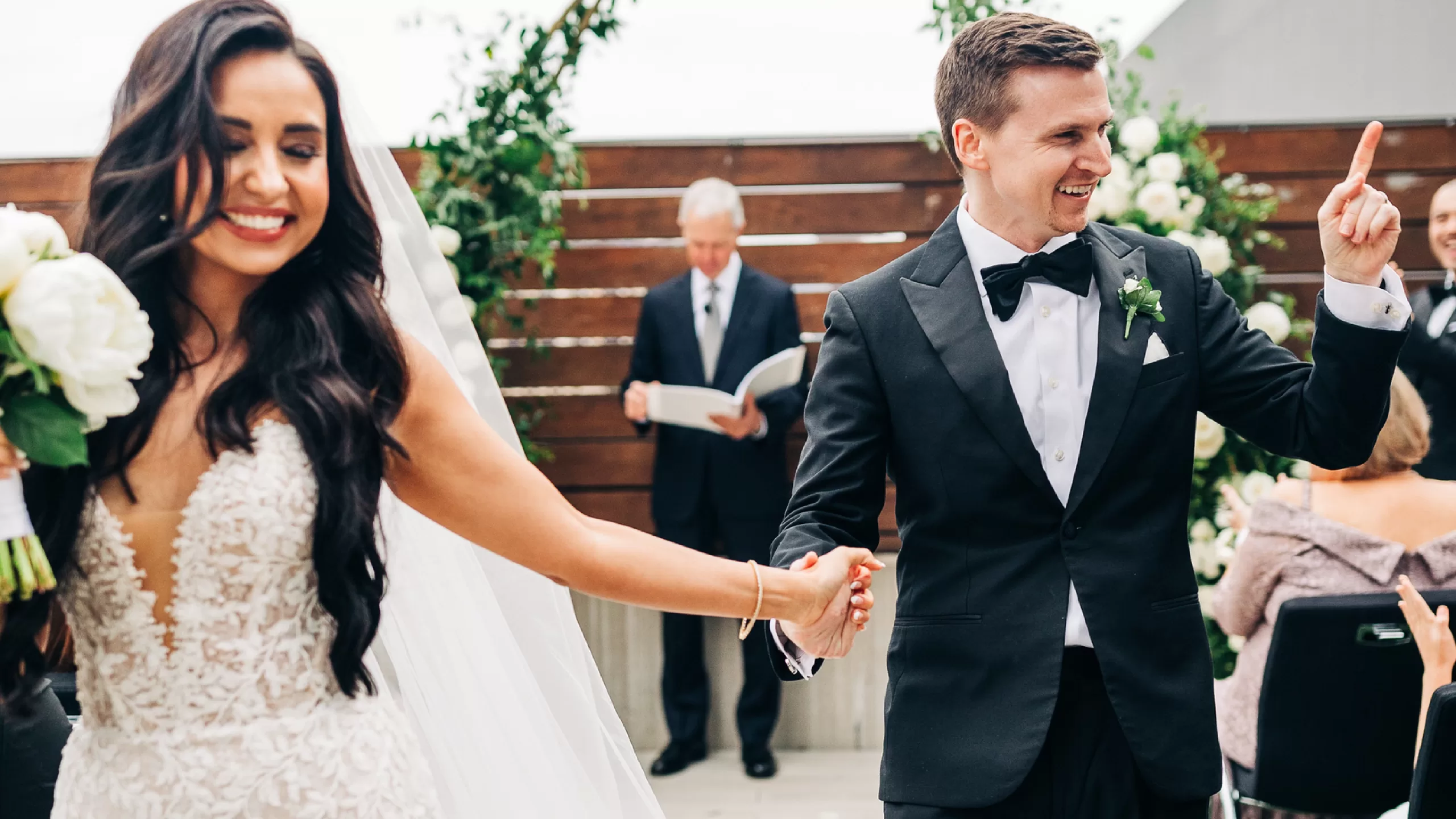 A bride and groom smiling and holding hands after an outdoor wedding ceremony.